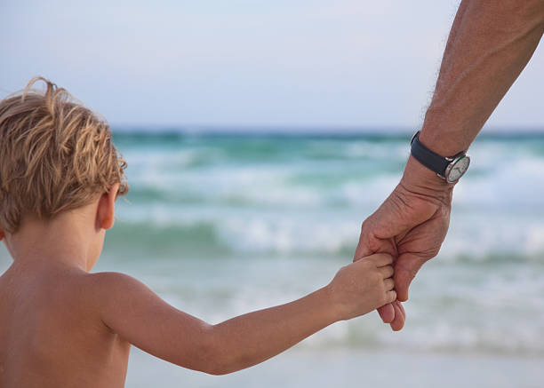 istock Little boy holding a man's hand at the beach 182145392
