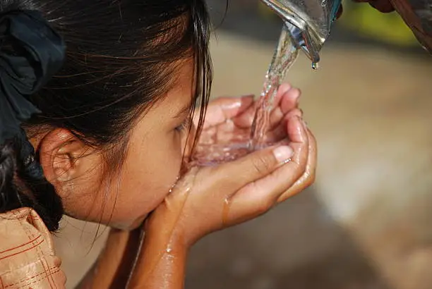 Photo of Small dark haired child drinking water using her hands