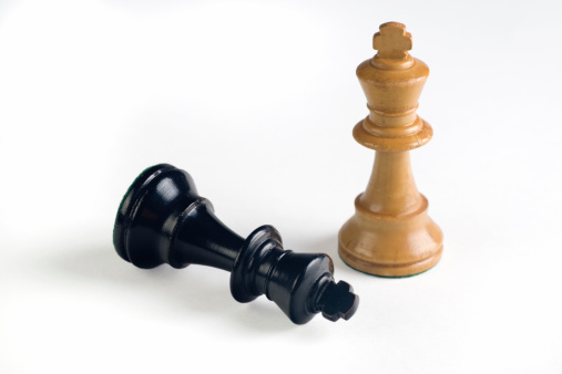 upright white chess king with black king tipped over