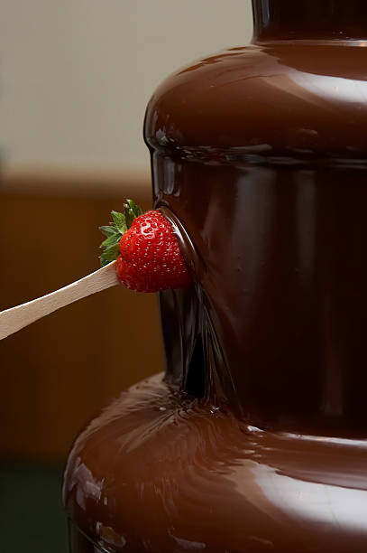 chocolate waterfall tower with a strawberry being coated by the running chocolate. You can see the hand holding the strawberry in the reflection of the chocolate 