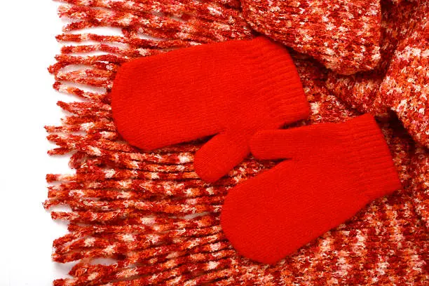 A pair of red winter mittens lying on a scarf