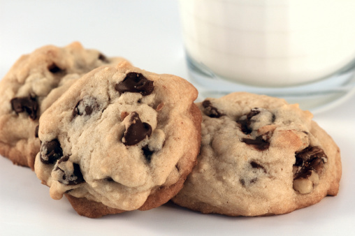 Homemade chocolate chip walnut cookies with a glass of milk in the background.