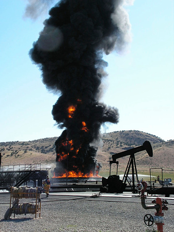 Large Fuel Pit Training Fire with smoke plume at a fire training center in Arizona. Oil rig structure and scaffolding visible.
