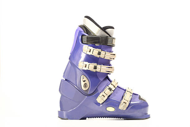 Orange alpine ski boots with four buckles in ski binding. One shoe is completely fastened to the ski, a second just put in binding.
