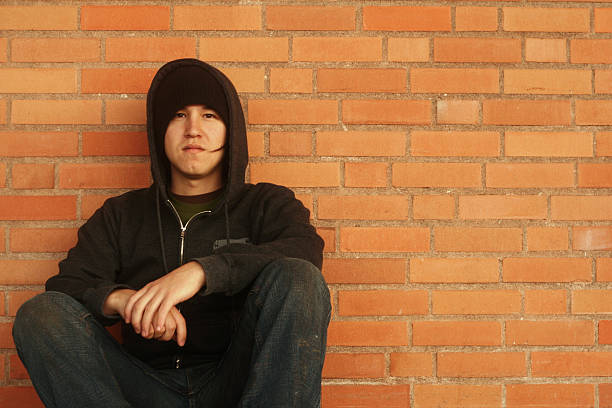istock Teenage boy dressed in black crouched down on brick wall  182147025