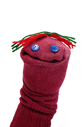 No childhood is complete without this classic kid craft project, the sock puppet. This adorable puppet was created at summer camp with mom's old red sock, glued on blue buttons for eyes and red and green yarn stapled on for groovy hair. Puppeteer wears it on hand with sock toe pulled in for mouth and ultimate personality. This puppet is isolated on a white background.