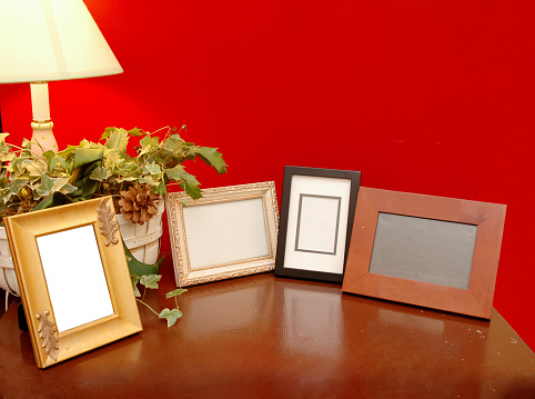 Brown table with 4 empty photo frames against a red wall.
