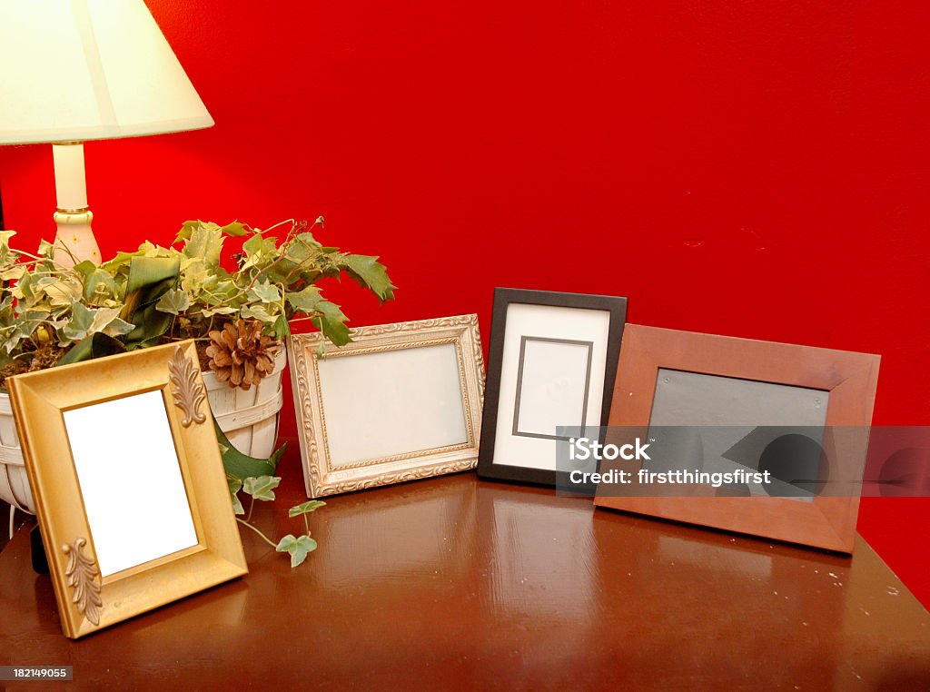 A wooden table adorned with empty picture frames Brown table with 4 empty photo frames against a red wall. Picture Frame Stock Photo