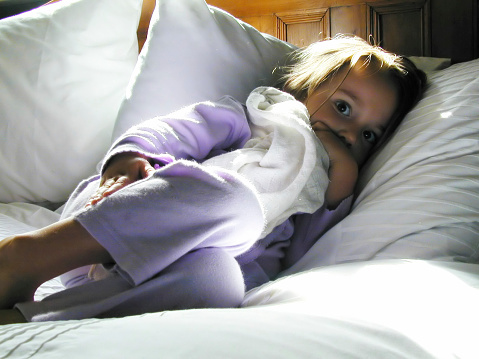 A young girl lies on a white pillow. Sucking her thumb..Similar images :-