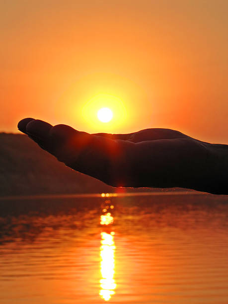 A male hand holding the sun declining above a river