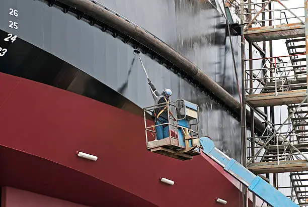 Man painting ship with copper-based paint in dry dock