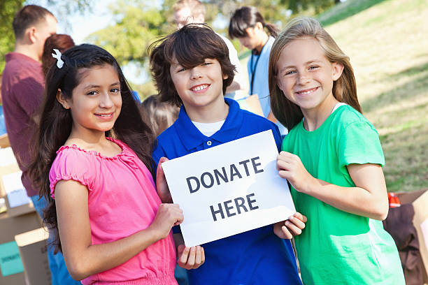 istock Three children holding a donate here sign at donation center 182151779