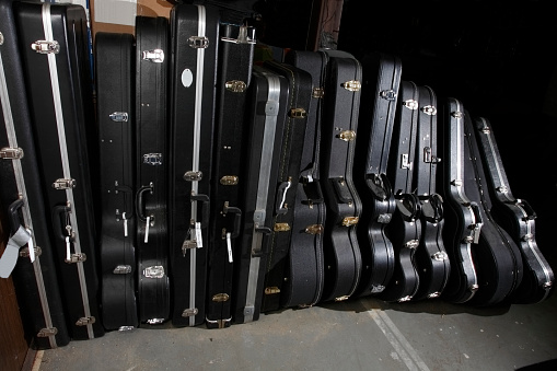 A row of 16 different black guitar cases standing in a storage area. argb profile.