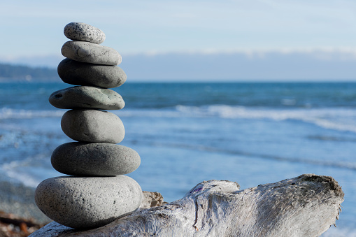 An image of several stones stacked and balanced carefully with the blue Pacific Ocean in the background.