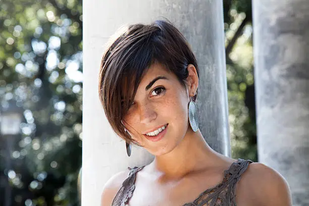 Beautiful girl standing by Roman columns smiling at the camera.