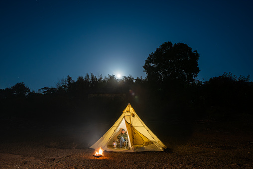A man in a tent at night with a campfire next to him