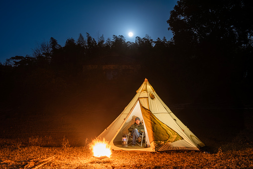 A man in a tent at night with a campfire next to him