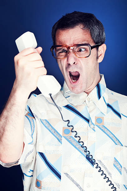 One middle aged nerd angry because of an inopportune phone call. He is yelling at the receiver and making a face. Made in a professional photo studio. Vertical format.