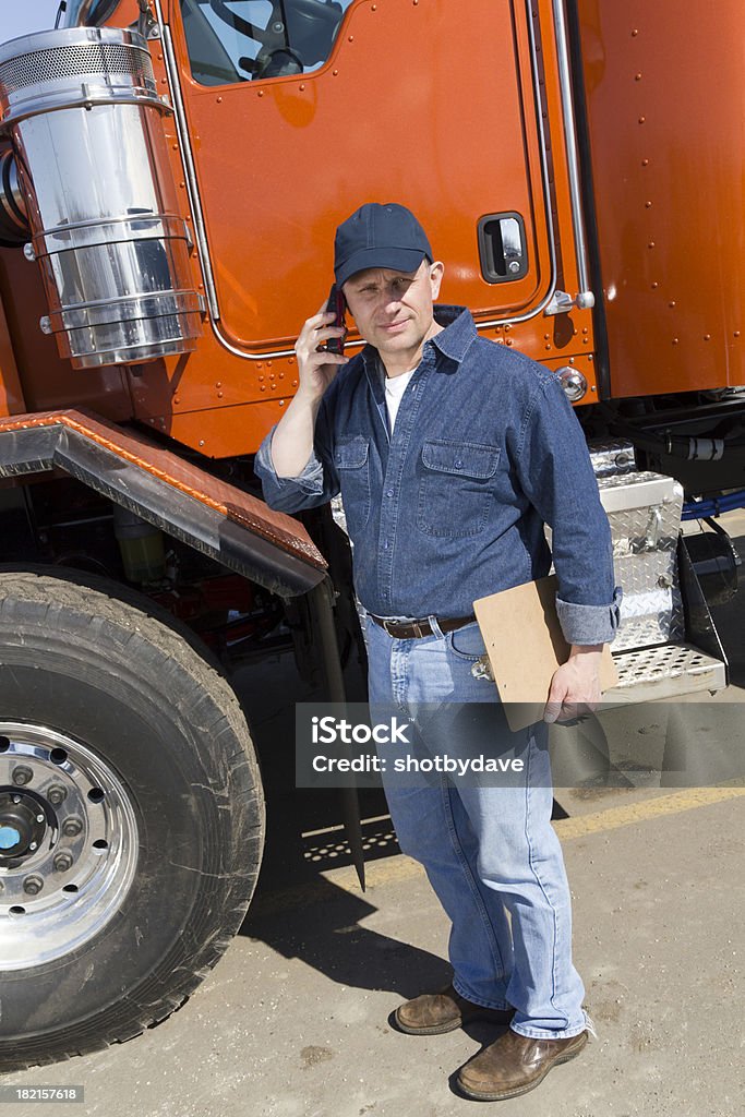Truck Driver and Orange Semi A  royalty free image from the transportation industry of a truck driver on the phone next to his orange semi. Driver - Occupation Stock Photo