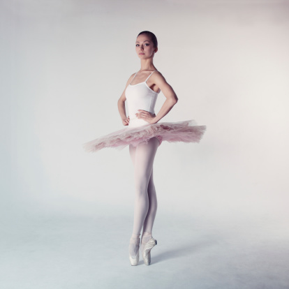 Young ballerina in pointe shoes practicing dance moves on pink background, closeup. Space for text