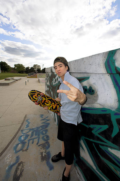 istock Young Asian skateboarder making peace sign at skate park. 182160663
