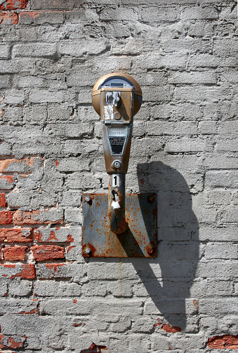 An old parking meter attached to a decaying brick wall.