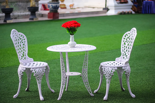 Table with red rose flowers in vase and blank two chair on green grass floor background