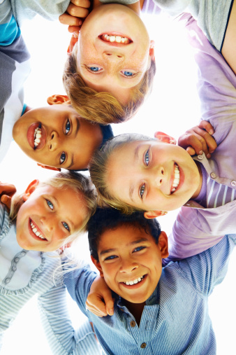 Low angle view of cheerful children huddling together with arm around
