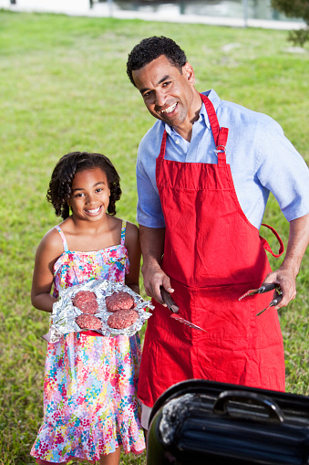 African American father, 40s, and daughter, 8 years, with barbecue grill.  Main focus on man.