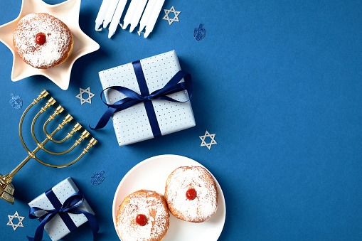 Happy Hanukkah card template. Flat lay golden menorah, gift boxes, jelly donuts, candles on blue background.