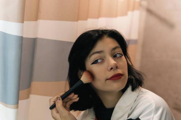 Portrait of Teenage Girl Contouring with Makeup Brush in Front of Mirror A close-up portrait of a teenage girl using a makeup brush to contour her face while looking into the mirror. The focus is on her reflection and the precision of her makeup application. teenage girl before and after make up stock pictures, royalty-free photos & images