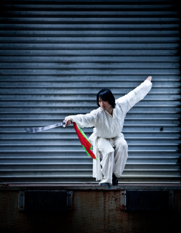 A kung fu warrior dressed all in white and practicing with the traditional sword (Kwan Do) of Kung Fu in an alley of New York City