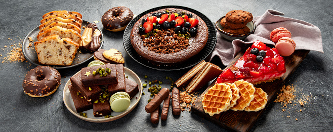 Tasty cake, cookies, waffles, macaroons, muffin. Delicious desserts on dark background. Food concept. Banner.