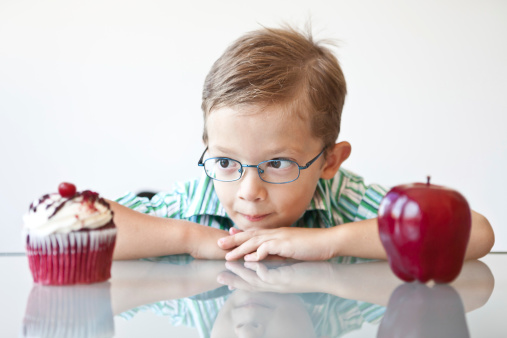 A little boy choosing between a cupcake and apple...looks like the cupcake is the winner.