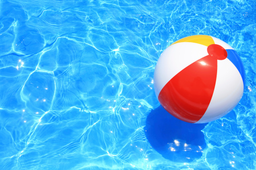 Beach ball floating in a pool with small waves reflecting in the summer sun.