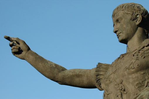 An isolated (on blue background) view from the bottom of a roman emperor Caesar Augustus statue made of green material with his finger pointing in one direction meaning power and commitment