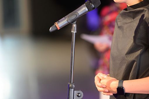 Hands of a woman standing behind a microphone at a public meeting, giving a speech, close-up, copy space