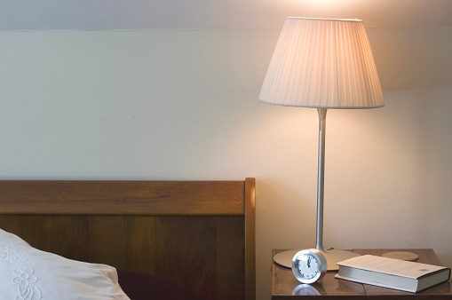 Walnut sleigh bed with side table. Lamp, book and alarm clock.