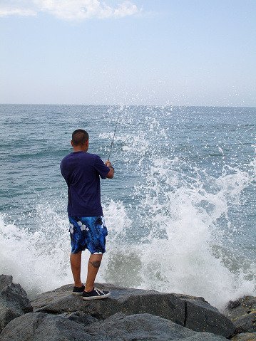 Young hispanic man fishes at Newport Beach jetty