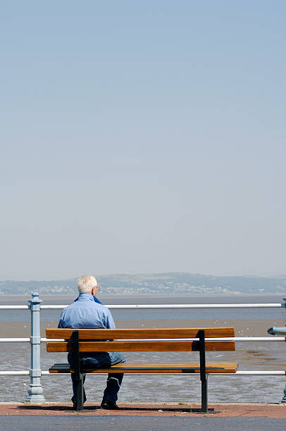 istock Retired man sitting on bench enjoying sea views 182172264