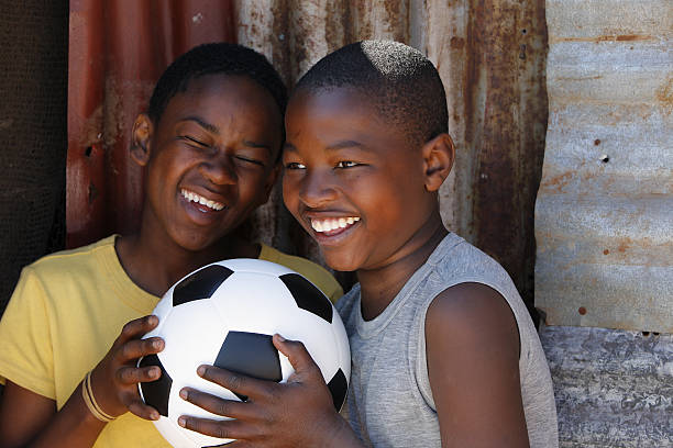Two African children enjoying a joke together whilst holding a new soccer ball in front of their humble shack dwelling. in rural South Africa.