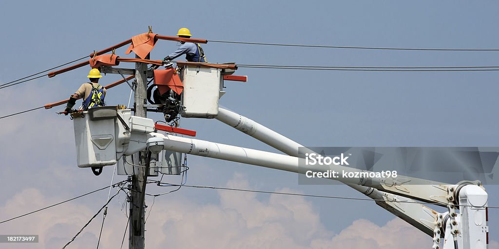 Two workers in a crane repairing a power pole Hydro workers work from boom buckets to restore power to a community. 2 to 1 aspect. Power Line Stock Photo