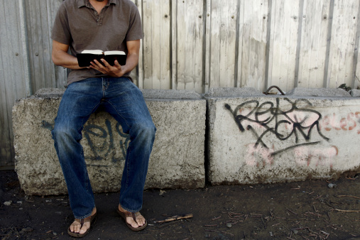 A man in an urban/industrial area reading the Bible.