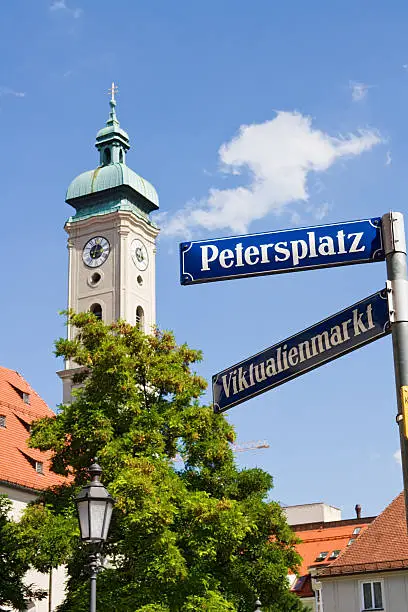 Street sign: Petersplatz and Viktualienmarkt. In the background the Heilig-Geist-Kirche. Selective focus on the sign.