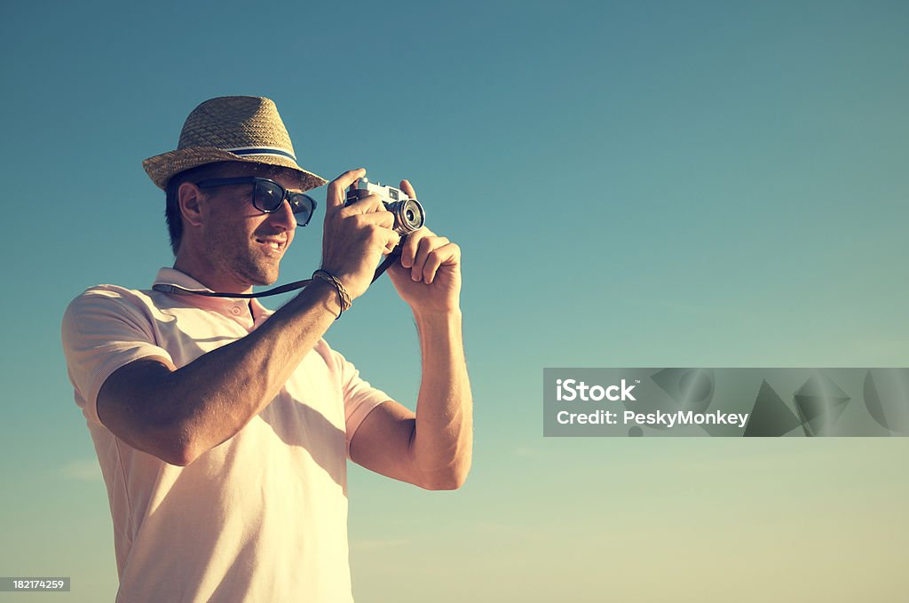 Retro Tourist Photographer Taking a Photo in Vintage Scene Retro tourist photographer with hat and sunglasses snaps a photo with an old fashioned point and shoot camera Adult Stock Photo