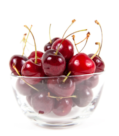 Bowl full of cherries on white background.