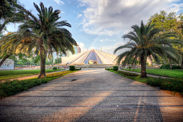 Enver Hoxha Pyramid in Tirana Tirana Albania: This national symbol was erected in 1985 by the daughter of the former communist dictator Enver Hoxha, with intentions of building a museum honoring the life of her father. Today the building awaits renovation and a new function. A rainbow can be seen emerging from right behind the pyramid after a brief rain storm. Photo processed for high dynamic range. albania photos stock pictures, royalty-free photos & images