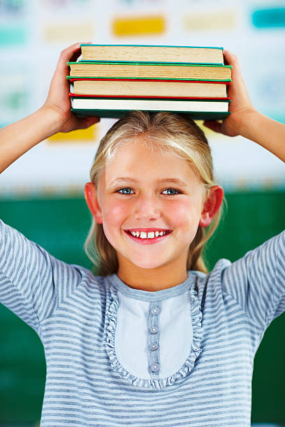 istock Schoolgirl holding a stack of books on her head 182174627