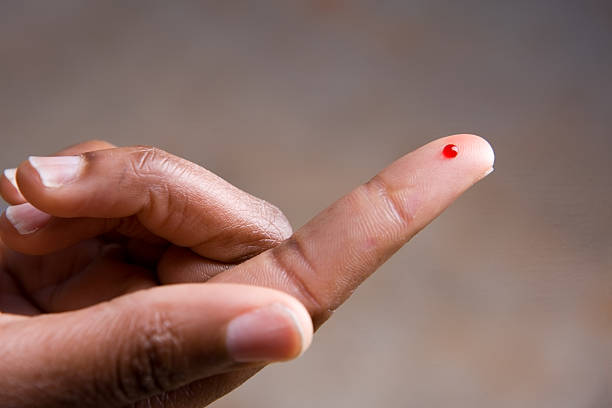 Drop of blood on fingertip for a medical exam A drop of blod on a young African American woman's fingertip.  She is preparing to perform a blood sugar test. blood drop stock pictures, royalty-free photos & images