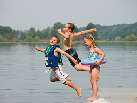 2 young boys and a young girl are jumping into a lake.  They have very happy faces and show alot of excitement